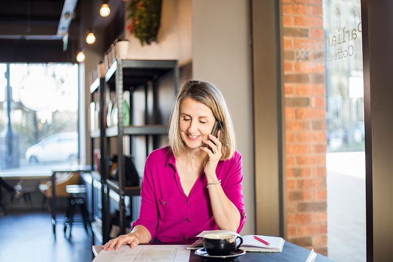 Women in pink blouse sitting at a table in a coffee shop taking a phone call